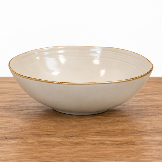 Four Candle Satchville stoneware salad bowl in cream with a rustic rim, set on a white wooden surface.